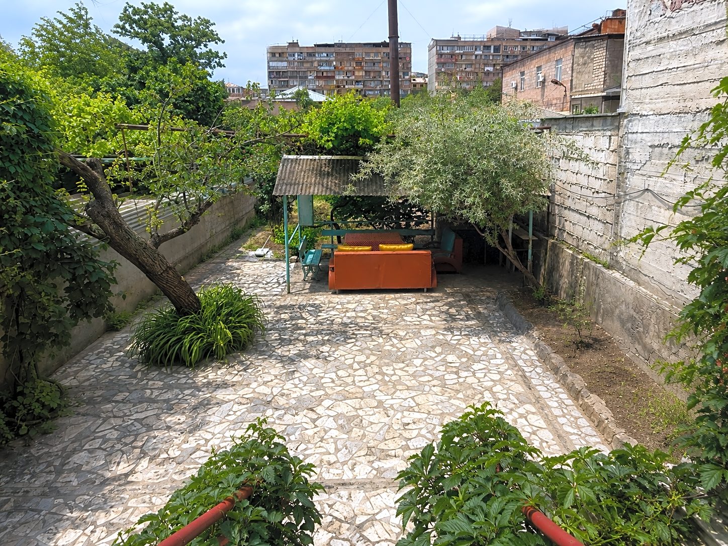 Gravel courtyard garden with an old vine, stone walls and an orange sofa