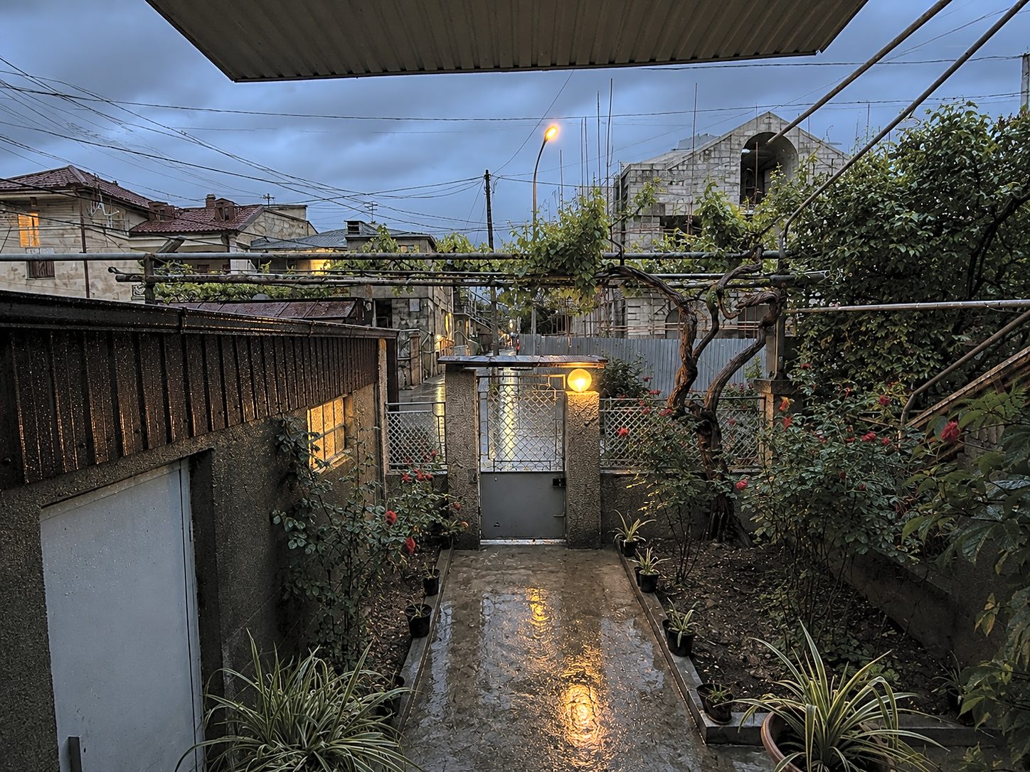 The gate passage at dusk with warm lights along the wet stone path