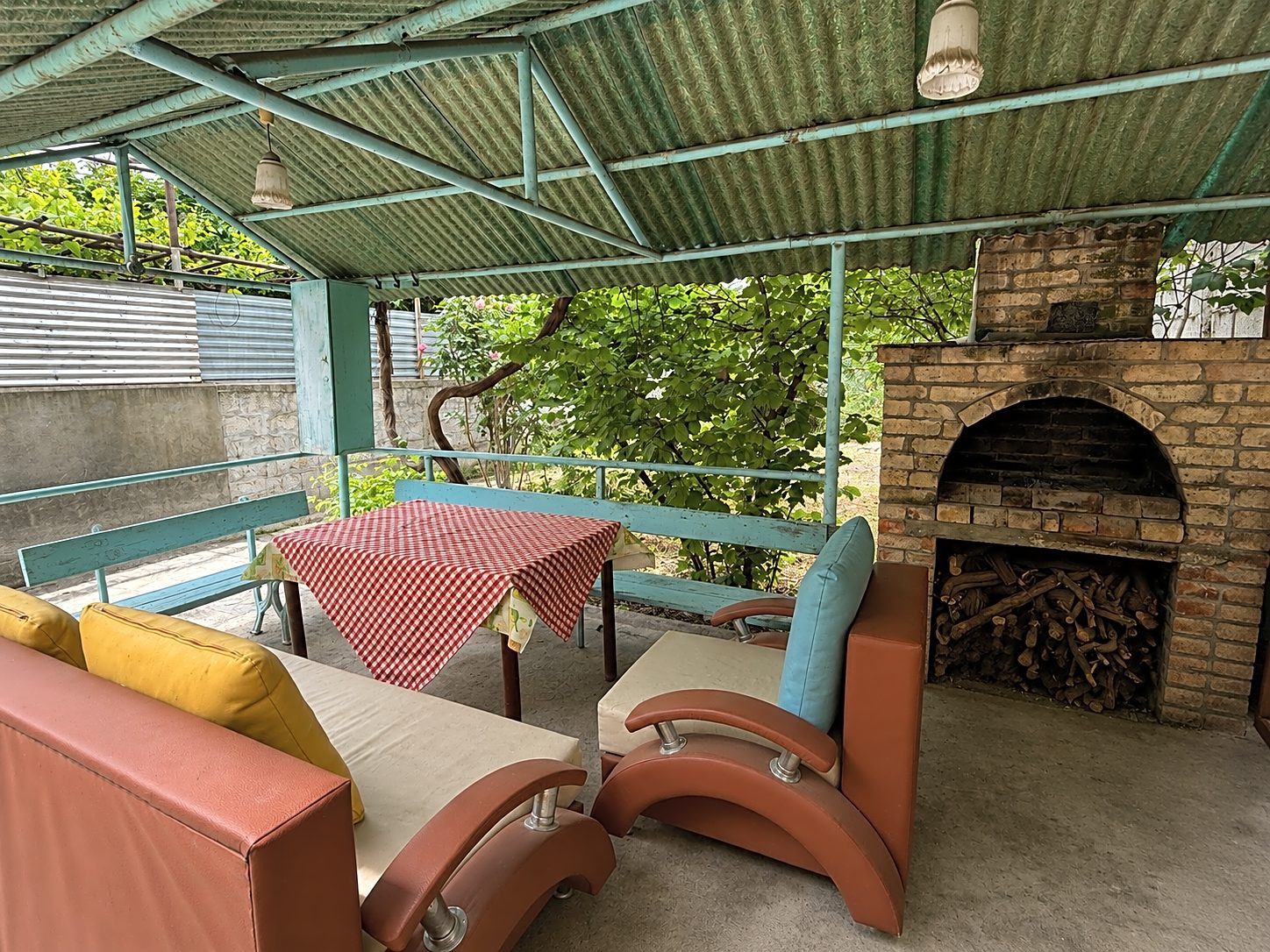 Covered garden terrace with colourful sofas and a brick barbecue